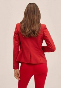 Veste rouge avec un design péplum, forme ajustée et poignets boutonnés. Associée à un pantalon rouge assorti. Tissu lisse avec une finition polie.