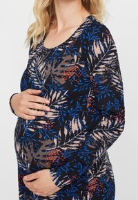 Langarm-Baumwolloberteil für Schwangere aus dehnbarem Material, mit einem dunklen blauen Hintergrund, der mit einem Blumenmuster in hellbeige und roten Akzenten verziert ist.
