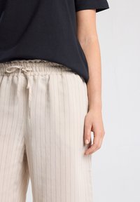 Beige striped pants with an elastic waistband and adjustable drawstring, made from lightweight fabric. Paired with a black short-sleeve top.