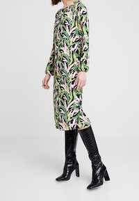 Floral dress with green, pink, and black leaves; long sleeves, knee-length, round neckline, paired with shiny black knee-high boots.