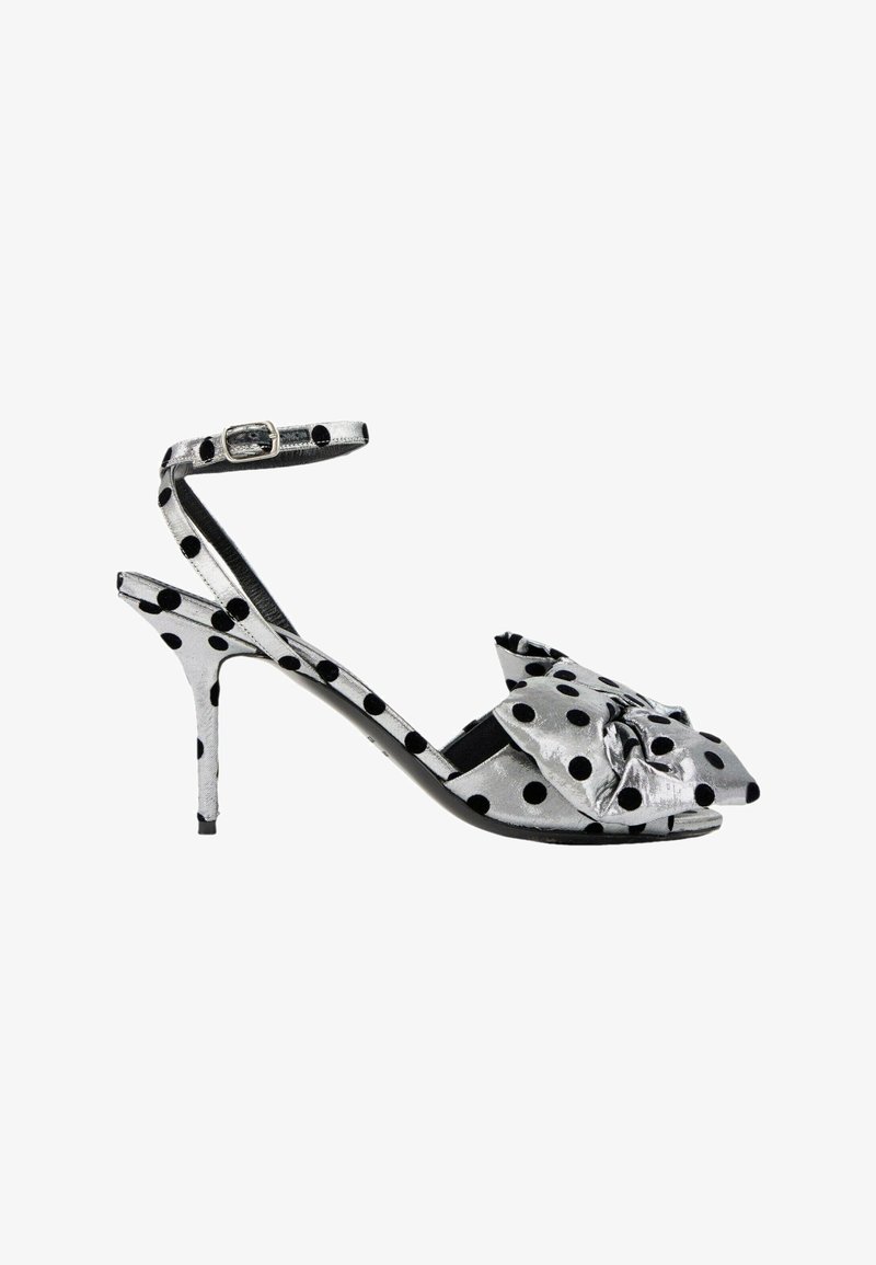 Sandale à talons hauts argentée avec des pois noirs, bride cheville avec boucle et un grand détail nœud sur les orteils.