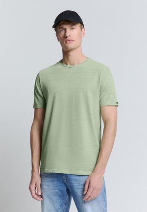 T-shirt à manches courtes vert clair avec des rayures horizontales, col rond et accent noir sur la manche, associé à un jean bleu clair.