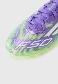 Lettvekts lilla fotballsko med en sikksakk grønn design, teksturert overflate og hvite detaljer med 'F50' merkevaren på siden.