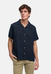 Camisa de lino de manga corta en azul marino con cuello, con botones de madera clara y un ajuste holgado, combinada con chinos de color claro.