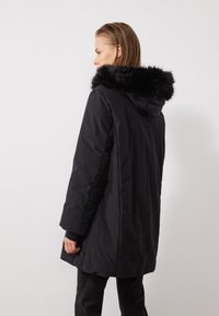 Geacă parka neagră cu glugă căptușită cu blană sintetică, mâneci până la umăr, croială largă și textură netedă, mată.