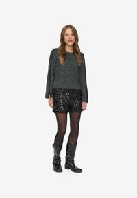 Grå strikket sweater med flared ærmer, parret med en sort pailletnederdel. Modellen bærer sorte knæ-høje støvler og sorte strømpebukser.