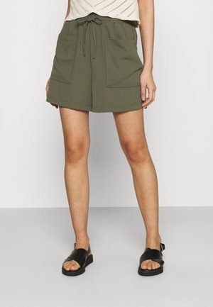 Shorts vert olive avec taille à cordon, présentant deux poches avant et une coupe décontractée, associés à des sandales noires à lanières.