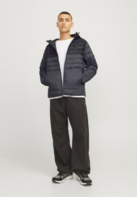 Black puffer jacket with horizontal stitching, front zipper, and hood; paired with dark loose-fitting pants and black athletic shoes.