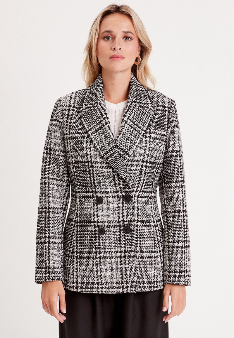 Double-breasted jacket in black and white houndstooth pattern, featuring a notched collar, long sleeves, and black buttons. Textured fabric.