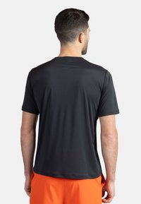 Svart atletisk t-shirt med korta ärmar, slät textur, rund nacke, enkel design och flexibel passform. Bärs med orangea shorts.