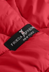 Rode pufferjas met een zwart etiket met "FRIEDA & FREDDY" en een hondenlogo, met nadruk op glossy materiaal en een gestikte textuur.