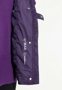 Lila wasserdichte Jacke mit strukturiertem Strickkragen, Druckknöpfen und Branding am Ärmel. Leichtes, glattes Außenmaterial.