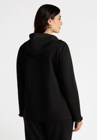 Sudadera negra con capucha y mangas largas, de textura suave y con adornos de cuentas decorativas en los puños. Diseño de corte recto.