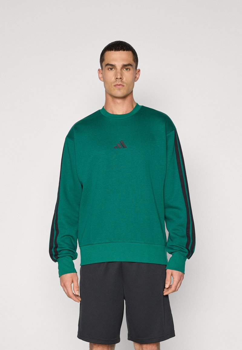 Grøn sweatshirt med tekstureret overflade, rund halsudskæring og sorte stribe detaljer på ærmerne. Har et lille sort logo på brystet.