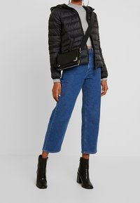 Abrigo acolchado negro con capucha, camiseta gris, jeans de pierna ancha azul y botas de tobillo negras con tacón. Bolso bandolera con detalles plateados.