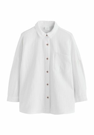 Biała koszula z długim rękawem zapinana na guziki, z przednią kieszenią i brązowymi guzikami, o luźnym kroju i fakturowanej tkaninie.