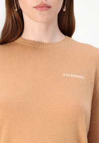 Tan knitted sweater with a crew neck, featuring a small white logo "2ND DAY" on the left side. Soft texture and ribbed detailing.