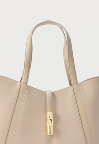 Μπεζ δερμάτινη τσάντα με υφή, με διπλούς ιμάντες και ορθογώνιο κούμπωμα σε χρυσό τόνο, σε απλό λευκό φόντο.