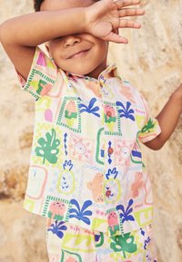 Kurzärmeliges Hemd mit Kragen und passende Shorts in Pastellfarben mit verspielten Mustern von Tieren, Pflanzen und geometrischen Formen.