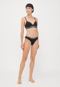 Black lingerie set featuring a padded bralette and low-rise panties. Soft fabric with contrasting logo band detailing along edges.