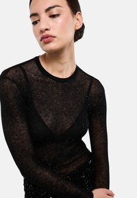 Haut noir transparent à manches longues avec une texture côtelée et des sequins éparpillés, présentant un col rond et une silhouette ajustée.