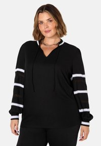 Schwarzes Oberteil mit V-Ausschnitt und Kordeln. Lange Ärmel mit weißen und durchsichtigen Spitzenstreifen. Weicher Stoff mit entspannter Passform.