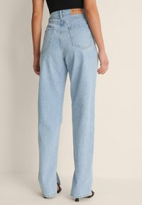 Vaaleansiniset korkeavyötäröiset farkut, joissa on suora lahkeiden malli, viisi taskua ja ruskea merkkilappu vyötäröllä. Hieman kulutettu pinta.