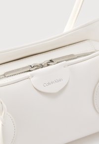 Λευκή δερμάτινη τσάντα Calvin Klein με διπλό ασημένιο φερμουάρ και εμφανές λογότυπο της μάρκας στην μπροστινή πτυχή.
