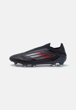 Crampon de football noir avec des accents rouges, présentant un design élégant, une tige texturée et six pointes coniques pour une traction sur le terrain.
