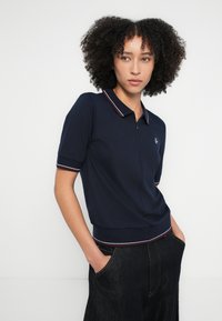 Tengerészkék rövid ujjú galléros póló bordázott gallérral és csíkos részletekkel; testhezálló kialakítás, kis logóval a bal mellrészen.