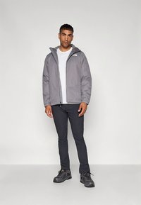 Gray waterproof jacket with a hood, white t-shirt underneath, paired with dark pants and black hiking shoes, standing on a neutral background.