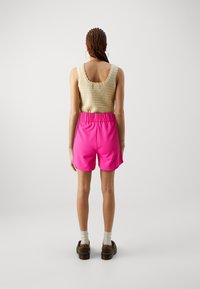 Débardeur beige en tricot avec encolure festonnée, accompagné d'un short rose élastiqué. Le modèle porte des chaussures compensées marron avec des chaussettes crème.