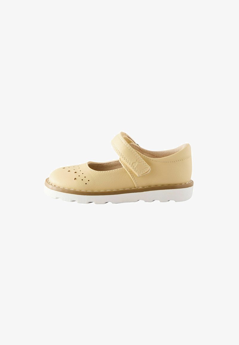 Light beige children’s Mary Jane shoe with perforated toe, adjustable hook-and-loop strap, and white ridged sole.