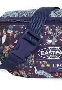 Marinblå blommönstrad tygväska med justerbar rem i mörkblått och plastspänne, som visar Eastpak- och Liberty London-märken.