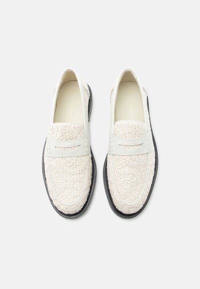 Mocassins blancs texturés avec des brides lisses et des semelles noires, vus de dessus sur un fond blanc uni.