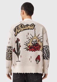 Πλεκτό πουλόβερ σε κρεμ χρώμα με πολύχρωμα κεντήματα, που περιλαμβάνουν λουλούδια, ένα κρανίο και λεπτομέρειες με λεοπάρ μοτίβο. Λεπτομέρεια με ξεφτισμένο τελείωμα.