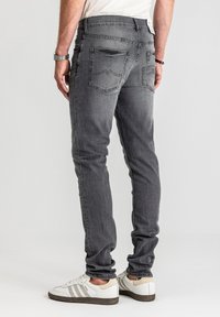 Szare dżinsy denimowe o dopasowanym kroju, z delikatnym wyblaknięciem, tylnymi kieszeniami z przeszyciami oraz podwiniętymi mankietami, zestawione z białymi trampkami.