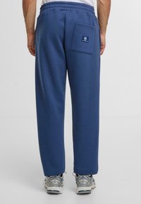 Marineblauwe joggingbroek met een elastische tailleband, een achterzak en een zachte textuur, gecombineerd met grijze en blauwe sportschoenen.