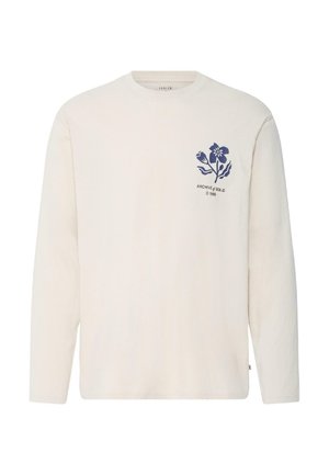 Kremi spalvos ilgomis rankovėmis marškinėliai su apvalia iškirpte, ant krūtinės kairėje mažas mėlynos gėlės piešinys ir užrašas „ARCHIVE of SOLID © 1999“.