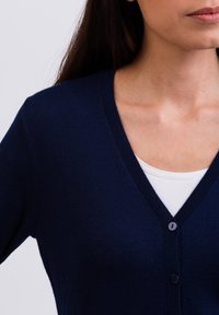 Námořnicky modrý cardigan s designem do V a třemi knoflíky, vyrobený z měkkého materiálu. Má klasický střih a žebrovaný výstřih.