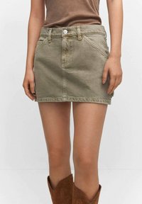 Olijfgroene denim mini-jurk met een rechte pasvorm, voorzakken, riemlussen en zilveren knoopdetail bij de taille. Zachte textuur, eenvoudig ontwerp.