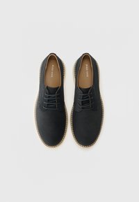 Schwarze Leder-Schnürschuhe mit runder Zehenpartie, kontrastierenden hellen Nähten und hellbraunen Innensohlen. Flache Gummisohlen bieten Stabilität.