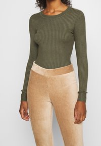 Haut à manches longues côtelé vert olive associé à un pantalon en velours côtelé marron clair taille haute, présentant des rainures verticales et une coupe ajustée.