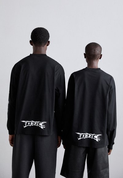 Black long-sleeve shirts with a loose fit. Both have a white graphic design at the back. Soft fabric with round necklines.