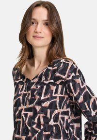 Top a maniche lunghe stampato in un tessuto leggero. Presenta una scollatura a V, un design astratto in nero, beige e rosso con una vestibilità ampia.