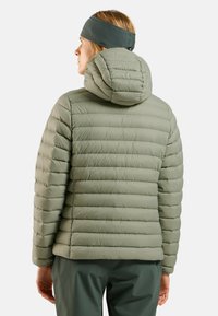 Green puffer jacket with horizontal quilted design, hood, and a smooth texture. Seen from the back, paired with matching dark green pants.