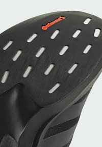 Suela de zapatilla negra con goma texturizada, que presenta recortes rectangulares blancos, forma curvada y el logotipo rojo "Continental".