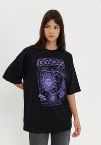 Black oversized cotton t-shirt featuring a purple graphic design of a sun and moon, with decorative floral elements and text.