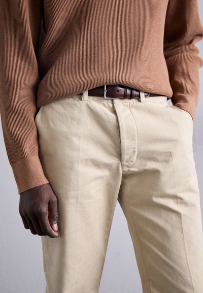 Beige bomullsbukser kombinert med en brun ribbestrikket genser, som har et brunt skinnbelte med en sølvspenne og en jevn tekstur.