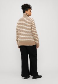Pulover oversized în dungi bej și alb, cu textură tricotată, guler înalt și tiv cu nervuri, asortat cu pantaloni largi negri și încălțăminte chunky neagră.